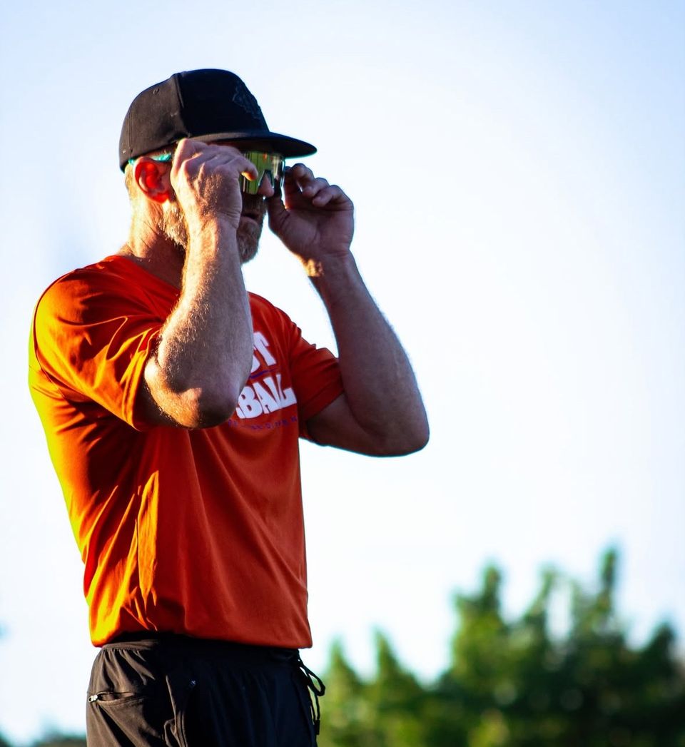 Kerry on the field in an orange coaching shirt, adjusting his sunglasses